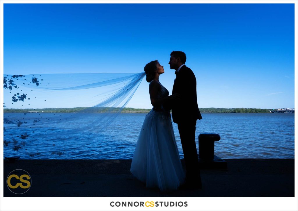 silhouette wedding portraits with bride and groom and flowing veil on sunny day near the Potomac River in old town Alexandria, Virginia photography by Connor Studios 