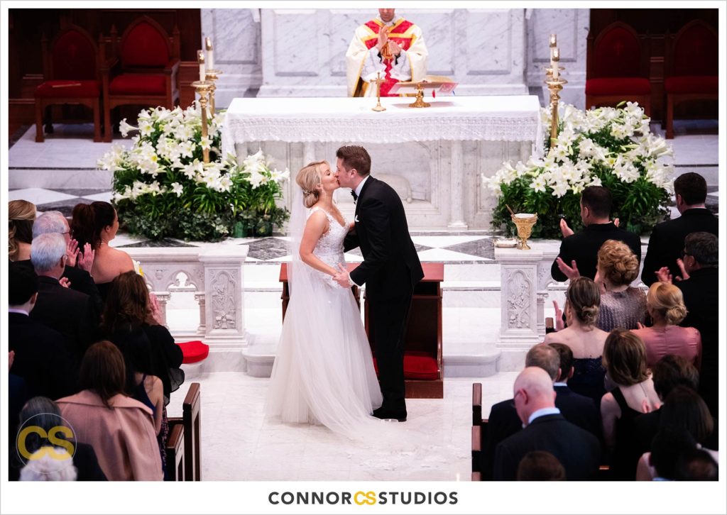 wedding ceremony and first kiss with bride and groom praying at The Basilica of St. Mary Church in old town Alexandria, Virginia photography by Connor Studios 