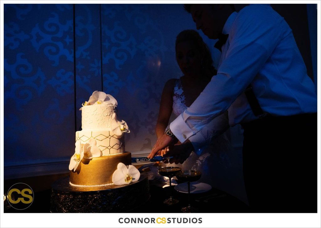 cake cutting during luxury wedding with candles and gold colors in the ballroom at Fairmont Hotel in Washington, DC photography by Connor Studios 