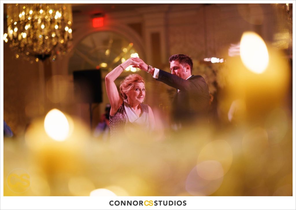 mother son dance during luxury wedding with candles and gold colors in the ballroom at Fairmont Hotel in Washington, DC photography by Connor Studios 