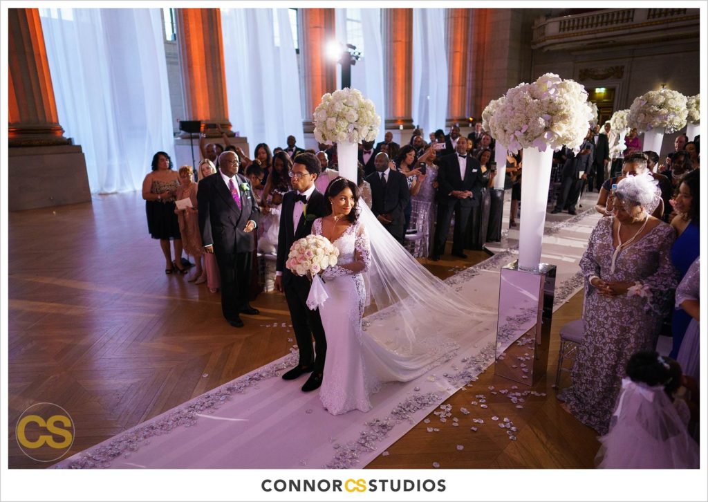 bride entering wedding at the Andrew W. Mellon Auditorium in Washington, DC by Connor Studios surrounded by tall white floral arrangements
