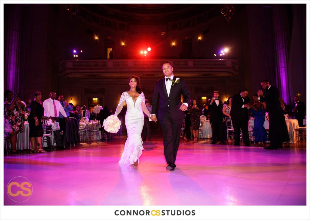 bride and groom entering their wedding reception in reds and purple at the Andrew W. Mellon Auditorium in Washington, DC by Connor Studios
