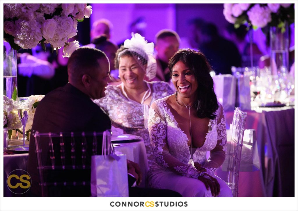 bride and groom laughing during speeches at wedding with purple and pink lighting at the Andrew W. Mellon Auditorium in Washington, DC by Connor Studios