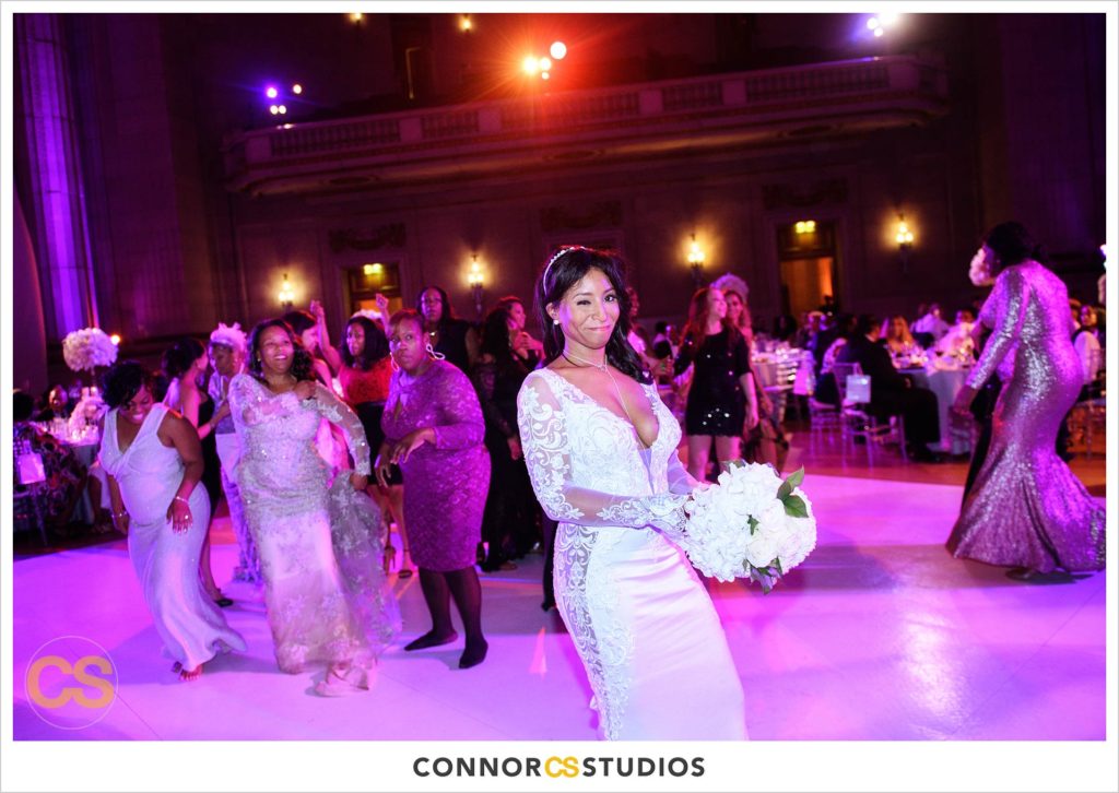bride and tossing bouquet at wedding with purple and pink lighting at the Andrew W. Mellon Auditorium in Washington, DC by Connor Studios