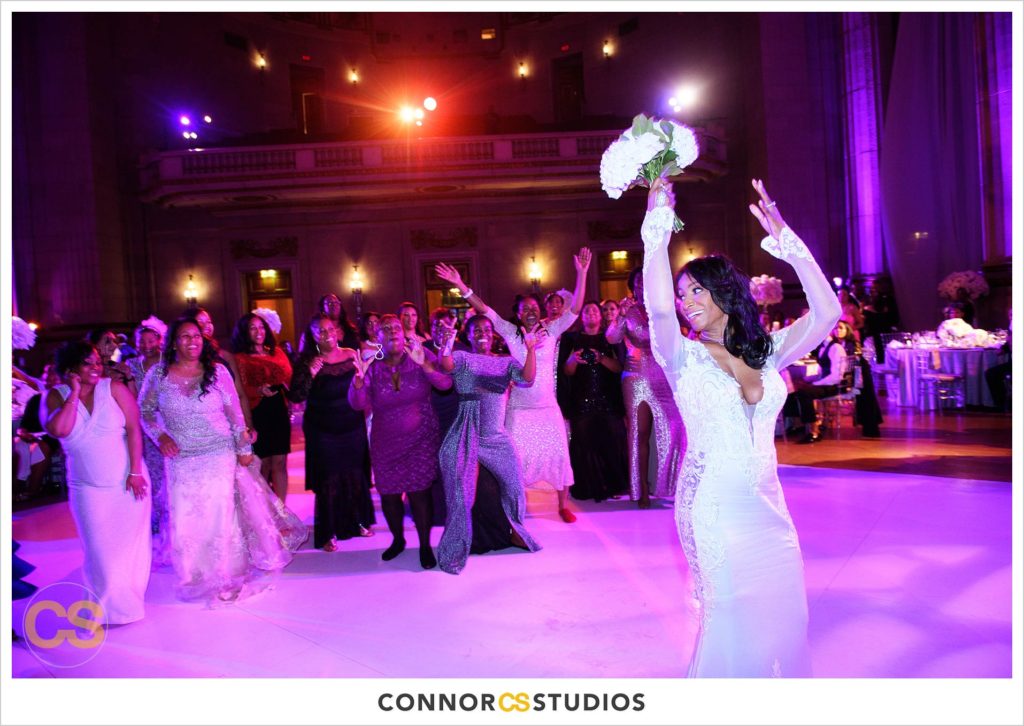bride and tossing bouquet at wedding with purple and pink lighting at the Andrew W. Mellon Auditorium in Washington, DC by Connor Studios