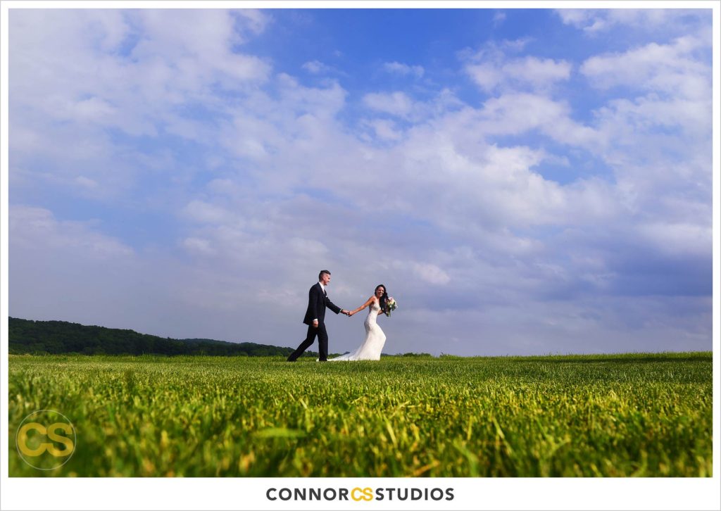 bride pulling groom through wide open field in the country at a wedding at wyndridge farm photography by connor studios