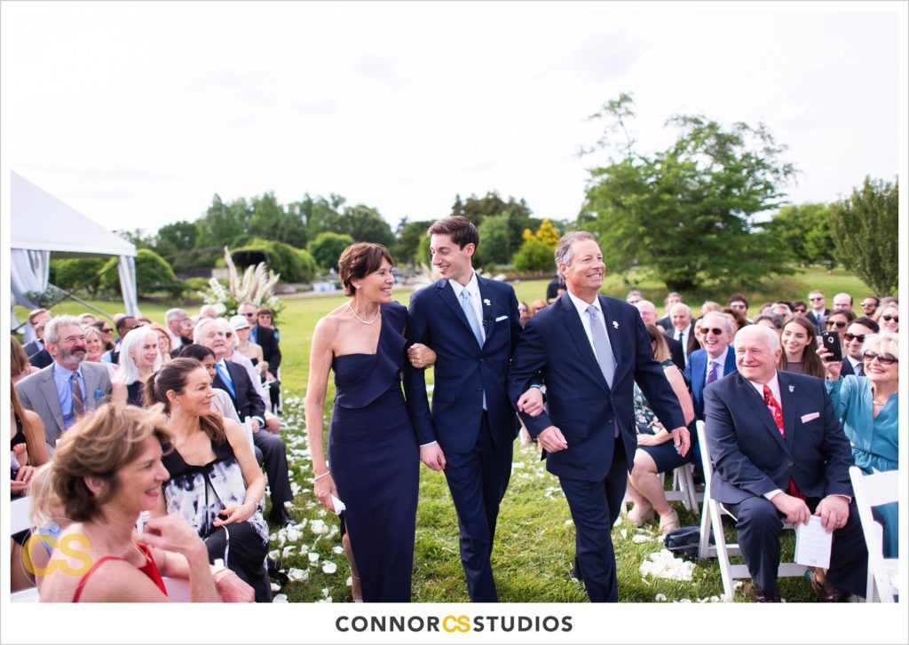 groom with parents walking down the aisle of his wedding ceremony outside at the national arboretum in washington, dc by connor studios
