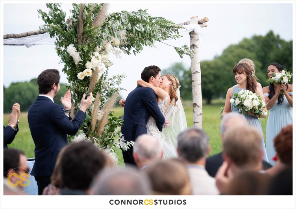 first kiss during outdoor summer wedding ceremony with the National Capitol Columns at the national arboretum in washington, dc by connor studios