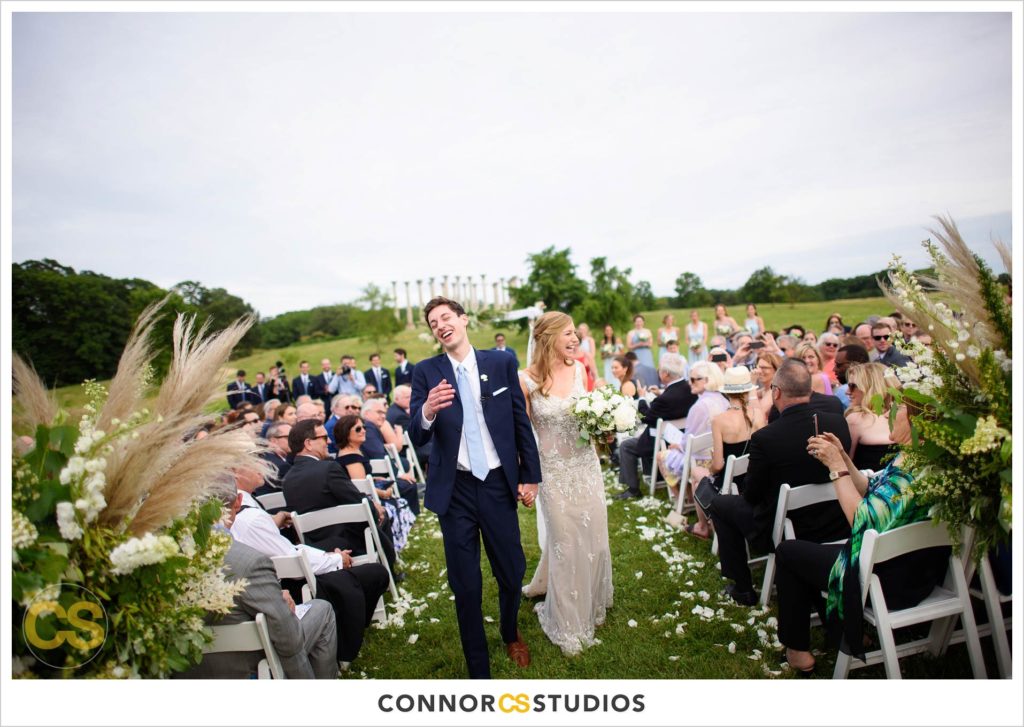 bride and groom walking down aisle during outdoor summer wedding ceremony with the National Capitol Columns in the background at the national arboretum in washington, dc by connor studios
